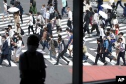 Seorang pria duduk di dekat jendela mengami orang-orang yang memakai masker berjalan di sepanjang penyeberangan pejalan kaki di distrik Shibuya, 30 September 2021, di Tokyo. (Foto: AP)