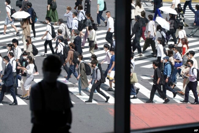Seorang pria duduk di dekat jendela mengami orang-orang yang memakai masker berjalan di sepanjang penyeberangan pejalan kaki di distrik Shibuya, 30 September 2021, di Tokyo. (Foto: AP)