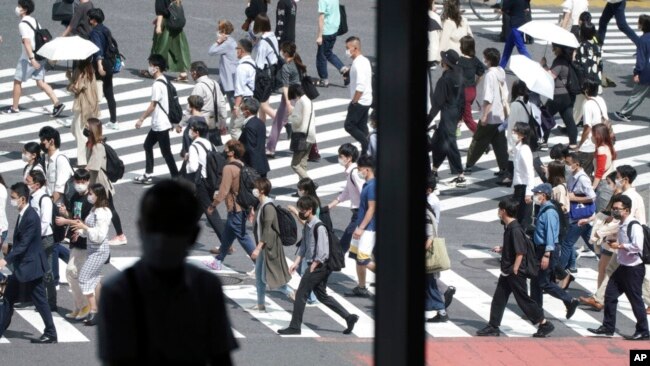 A man sits near a window as people wearing face masks walk along a pedestrian crossing at Shibuya district Sept. 30, 2021, in Tokyo.