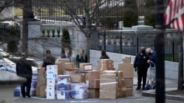 In this Jan. 14, 2021, file photo people wait for a moving van after boxes were moved out of the Eisenhower Executive Office building inside the White House complex in Washington.