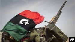 A Libyan rebel is covered up in the rebels flag next to his weapon as he moves on the road bewteen Al-Egila and Ras Lanuf, eastern Libya, Sunday, March 27, 2011