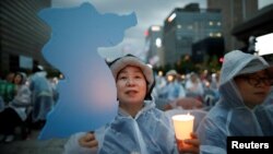 A woman holds a blue-colored cutout of the Korean Peninsula, symbolizing the unification of the two Koreas, during a candlelight vigil wishing for a successful summit between the U.S. and North Korea, in front of the U.S. embassy in Seoul, South Korea, June 9, 2018.
