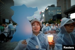 A woman holds a blue-colored cutout of the Korean Peninsula, symbolizing the unification of the two Koreas, during a candlelight vigil wishing for a successful summit between the U.S. and North Korea, in front of the U.S. embassy in Seoul, South Korea, June 9, 2018.
