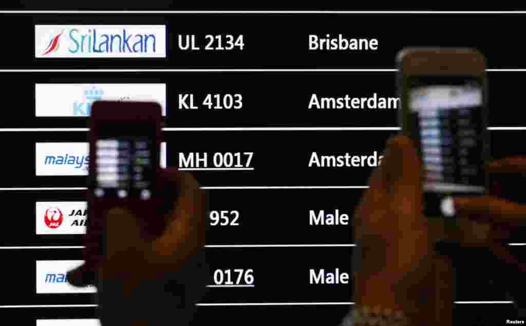 People take photos of a screen showing arrival details of Malaysia Airlines flight MH17 (C) at Kuala Lumpur International Airport in Sepang.