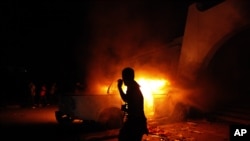 FILE - A Libyan civilian watches one of Ansar al-Shariah Brigades cars on fire, after hundreds of Libyans, Libyan Military, and Police raided the Brigades base, in Benghazi, Libya, Sept. 21, 2012.