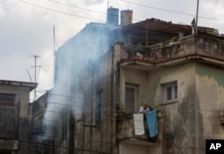 A man stands outside on his balcony as soldiers fumigate inside his home in Havana, Cuba, Feb. 22, 2016.