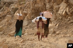 FILE - Yemenis carry relief supplies as they walk along a path outside the city of Taiz, Yemen, Jan. 17, 2016.