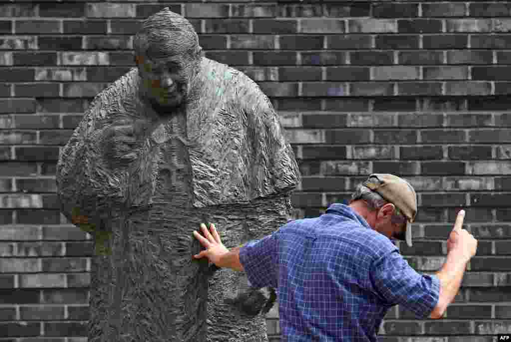 A worker installing the bronze statue of Pope John Paul II at St. Mary's Cathedral in Hangburg, Germany gestures.
