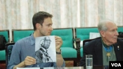 Military history author Adam Makos, seated next to Thomas Hudner, shows North Korean army officers a photo of US Navy pilot Jesse Brown who crash landed his plane in their country in 1950, in Pyongyang, July 22, 2013. (Photo: Steve Herman / VOA)