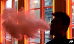 FILE - A patron exhales vapor from an e-cigarette at the Henley Vaporium in New York