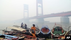 FILE - A woman disembarks from a boat as the Ampera Bridge is shrouded in haze from wildfires in Palembang, South Sumatra, Indonesia.