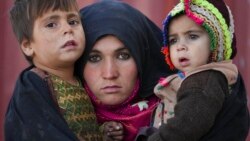 FILE - An Afghan woman holds her children as she waits for a consultation outside a makeshift clinic at a sprawling settlement of mud brick huts housing those displaced by war and drought near Herat, Afghanistan, Dec. 16, 2021.