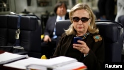 FILE - Then U.S. secretary of state Hillary Clinton checks her mobile phone aboard a military C-17 plane, Oct. 18, 2011.