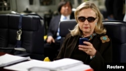 FILE - Then U.S. secretary of state Hillary Clinton checks her mobile phone aboard a C-17 military plane, Oct. 18, 2011.