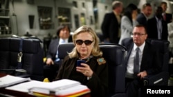 FILE - Then US secretary of state Hillary Clinton checks her mobile phone upon her departure in a military C-17 plane from Malta bound for Tripoli, Libya, Oct. 18, 2011.