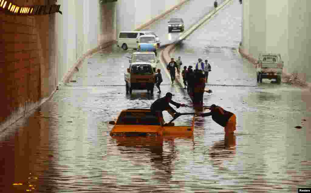 A man whose car is stuck in a flooded tunnel gets help from another man in Sana'a, Yemen.