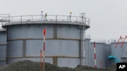 FILE - Workers wearing protective gears stand on the water tank that stores contaminated water at the Fukushima Dai-ichi nuclear power plant in Okuma, Fukushima prefecture, northeastern Japan, Nov. 12, 2014. 