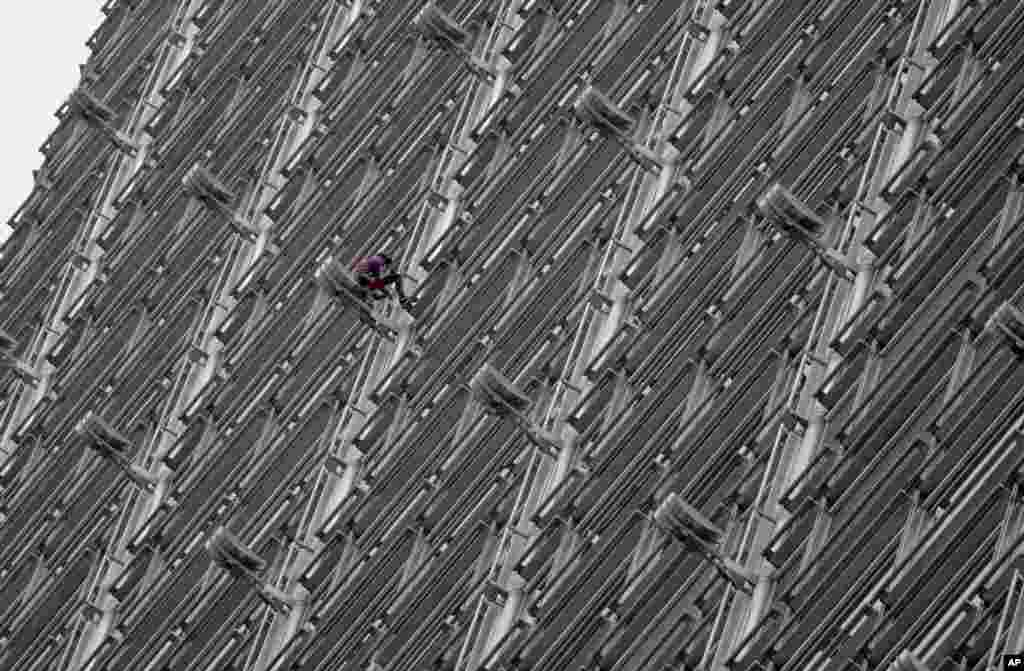 Alain Robert, a French rock and urban climber, hangs on to Cheung Kong Center building after hanging a large fabric displaying Chinese and Hong Kong flags, shaking hands and a shining sun in Hong Kong.