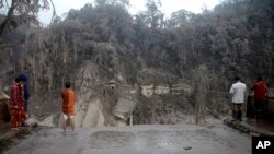 ຊາວບ້ານພາກັນເບິ່ງຂົວທີ່ເພພັງ ຈາກຫີນຮ້ອນ (ລາວາ) ທີ່ໄຫຼຜ່ານມາຈາກພູ ເຊເມຣູ ໃນເຂດເມືອງ ລູມາຈັງ ທາງພາກຕາເວັນອອກຂອງແຂວງ ຈາວາ ໃັນທີ 5 ທັນວາ 2021.