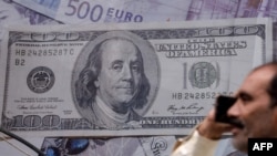 Un homme parle au téléphone devant un poster affichant des dollars américains à un bureau de change de Lahore, Pakistan, le 16 mai 2019. (Photo: ARIF ALI / AFP)