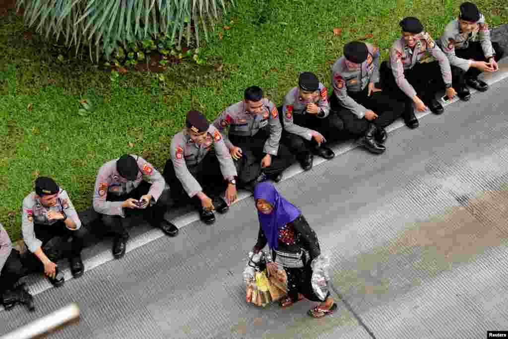 A street vendor carries her goods as Indonesian police officers rest during a May Day rally near the National Monument (Monas) in Jakarta, Indonesia.