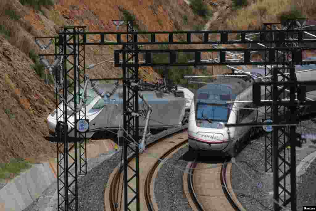 A passenger train passes by a wrecked train engine at the site of the train crash in Santiago de Compostela, northwestern Spain, July 26, 2013.&nbsp;