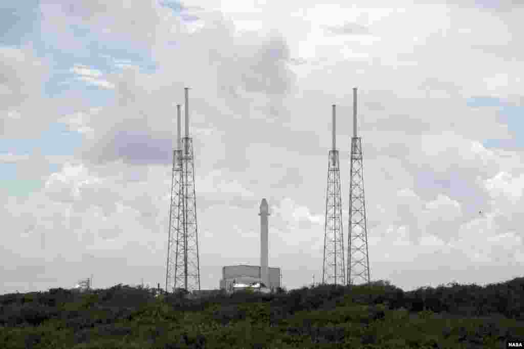 ຈະຫລວດ Falcon 9 ກັບເຄື່ອງບັນທຸກຍານອະວະກາດ Dragon ໄດ້ຖືກຕັ້ງໄວ້ຢ່າງໝັ້ນໃນທ່າຕັ້ງຂຶ້ນ ຢູ່ລະຫວ່າງກາງ ເສົາອາກາດທີ່ຮຸ່ງສະຫວ່າງສອງອັນຢູ່ເທິງແຜ່ນຂອງເຂດຍ່ານສົ່ງຍານອາວະກາດ Space Launch Complex 40, ທີ່ສະຖານີກອງທັບອາກາດ Cape Canaveral Air Force Station ລັດ Florida ໃນວັນທີ 7 ຕຸລາ, 2012. (NASA/Jim Grossmann)