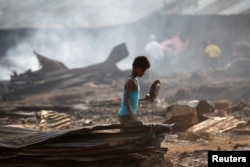 FILE - A boy searches for useful items among the ashes of burned-down dwellings at a camp for internally displaced Rohingya Muslims in Myanmar's western Rakhine state near Sittwe, May 3, 2016.