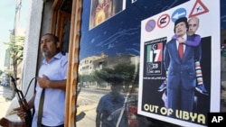 A Libyan rebel stands by a shop window decorated with a portrait of Moammar Gadhafi with his son Seif al-Islam on his shoulders, in Tripoli, Aug. 25, 2011