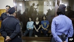 Feminist punk group Pussy Riot members, from left, Yekaterina Samutsevich, Maria Alekhina and Nadezhda Tolokonnikova sit in a glass cage at a courtroom in Moscow, Russia, August 17, 2012.