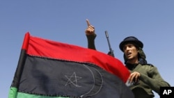 A rebel fighter gestures beside a Kingdom of Libya flag on a truck at a staging area to the east of Brega, April 4, 2011