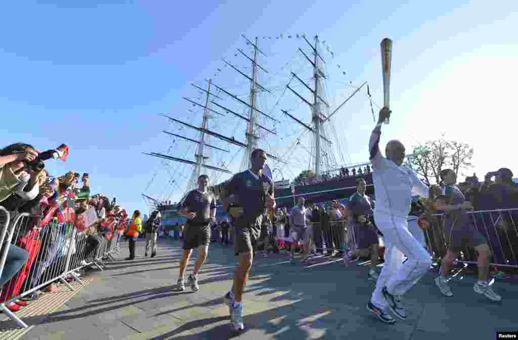 British around-the-world sailor Sir Robin Knox-Johnson carries the Olympic Torch around the restored Cutty Sark boat at Greenwich in London July 21, 2012. 