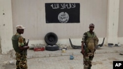 FILE - Soldiers stand at a checkpoint in front of a Boko Haram flag the Nigerian city of Damasak, Nigeria, March 18, 2015. In Senegal, 29 suspects are awaiting a ruling on terrorism-related charges. Most of the suspects are believed to have fought for Boko Haram in Nigeria, while others fought for jihadists in Libya and Mali.