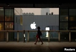 FILE - A woman walks past an Apple store in Beijing, China, July 28, 2016. Observers warn that the Trump administration succeeding in having Apple move manufacturing to U.S. soil would deal the Chinese economy a huge blow.