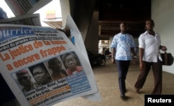 People walk past a man selling a copy of Le Nouveau Courrier, which has a picture of Ivory Coast's former first lady Simone Gbagbo (2nd L, on newspaper), in Abidjan, March 10, 2015.