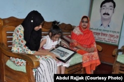 Two daughters of Sajedal Islam Sumon are looking at their father's years old photo. Sumon's wife (in orange clothing) is sitting at one corner in her house in Dhaka (28 NOV 2017).