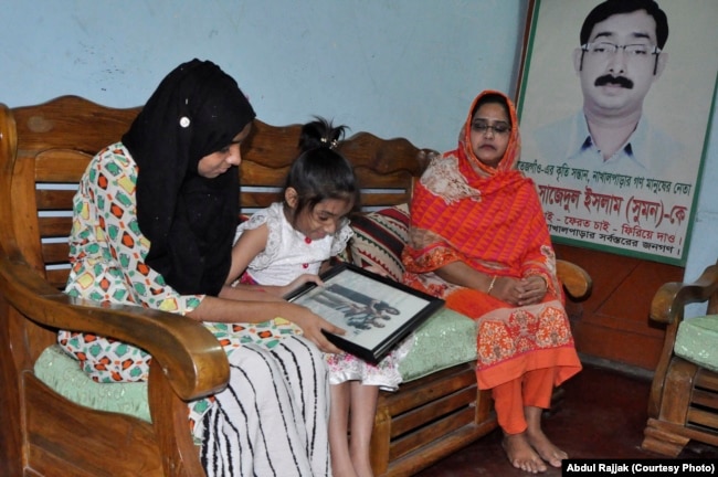 Two daughters of Sajedal Islam Sumon are looking at their father's years old photo. Sumon's wife (in orange clothing) is sitting at one corner in her house in Dhaka (28 NOV 2017).