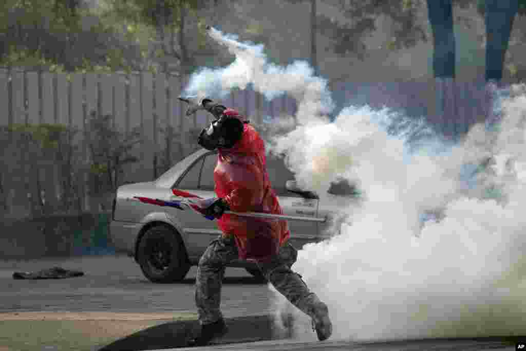 An anti-government protester throws back a tear gas canister at riot police during a clash at a sport stadium in Bangkok, Dec. 26, 2013.