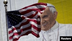 The U.S. flag flies in front of a mural of Pope Francis on the side of a building in midtown Manhattan in New York, Aug. 28, 2015.