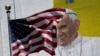 FILE - The U.S. flag flies in front of a mural of Pope Francis on the side of a building in midtown Manhattan in New York, Aug. 28, 2015.