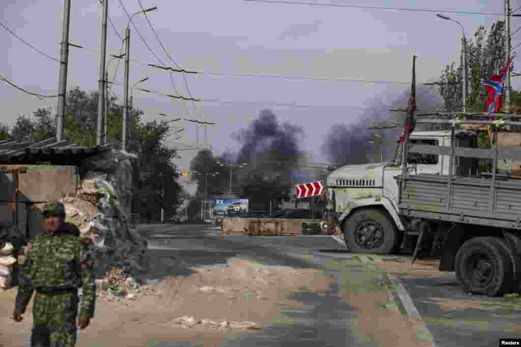 A pro-Russian rebel patrols a checkpoint as smoke rises near the Donetsk Sergey Prokofiev International Airport after recent shelling in Donetsk, eastern Ukraine, Sept. 23, 2014.