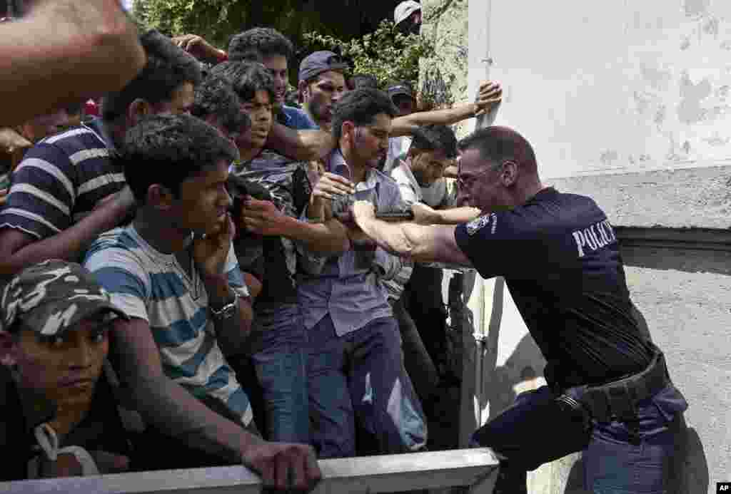 Seorang polisi Yunani mencoba menahan migran di balik pagar saat mereka menanti prosedur pendaftaran di sebuah stasiun polisi di pulau tenggara Kos. &nbsp;