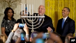 Israeli President Reuven Rivlin lights a menorah and sings, joined by President Barack Obama, first lady Michelle Obama and Nechama Rivlin, in the background, during a Hanukkah reception in the East Room of the White House in Washington, Dec. 9, 2015.
