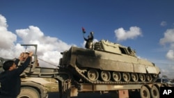 A rebel stands atop a destroyed tank, belonging to forces loyal to Libyan leader Muammar Gaddafi, after a coalition air strike, along a road between Benghazi and Ajdabiyah, March 21, 2011