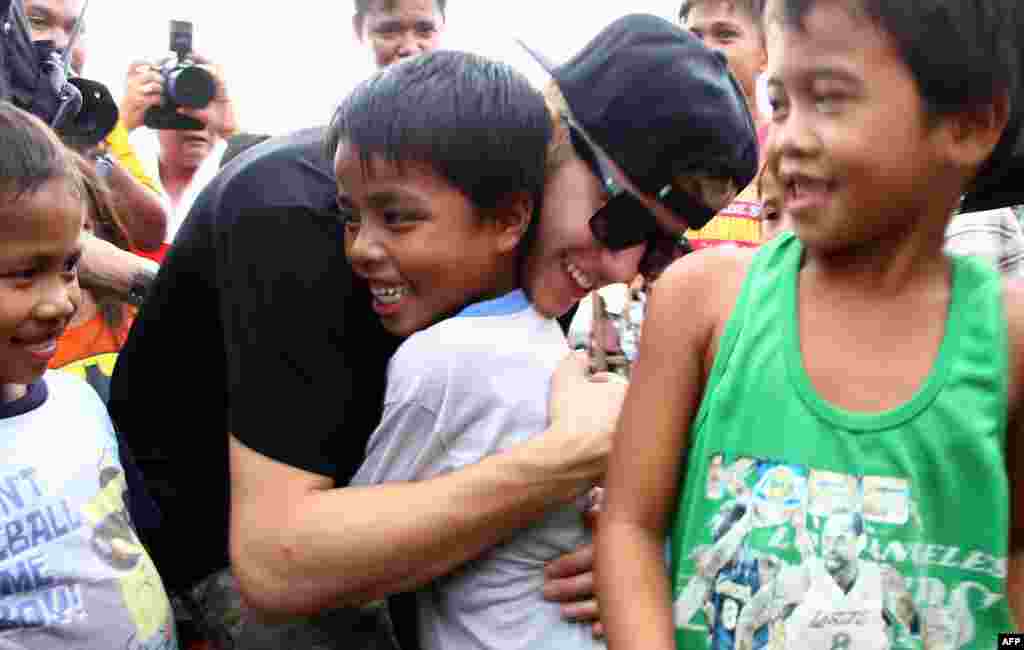 Penyanyi Kanada, Justin Bieber (tengah) memeluk seorang anak yang selamat dari bencana topan Haiyan di kota Palo, provinsi Leyte, Filipina tengah. 