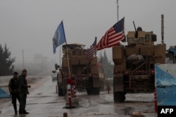 FILE - A line of U.S. military vehicles drive through a checkpoint of the Internal Security Forces in Manbij as they head to their base on the outskirts of the northern Syrian city, Dec. 30, 2018.