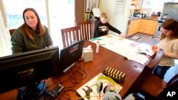 In this Tuesday, March 17, 2020 photo Kim Borton, left, works from home while her children Logan Borton, center, age 6 and Katie Borton, age 7, work on an art project in Beaverton, Ore. (AP Photo/Craig Mitchelldyer)