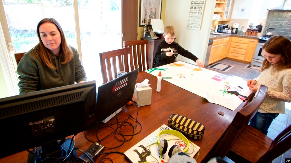 In this March 17, 2020 photo from Beaverton, Oregon, Kim Borton works from home while her children Logan, center, age 6 and Katie, age 7, as they work on an art project.