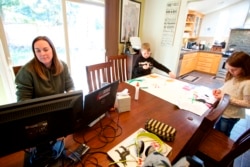 FILE - In this Tuesday, March 17, 2020 photo Kim Borton, left, works from home while her children Logan Borton, center, age 6 and Katie Borton, age 7, as they work on an art project in Beaverton, Ore.