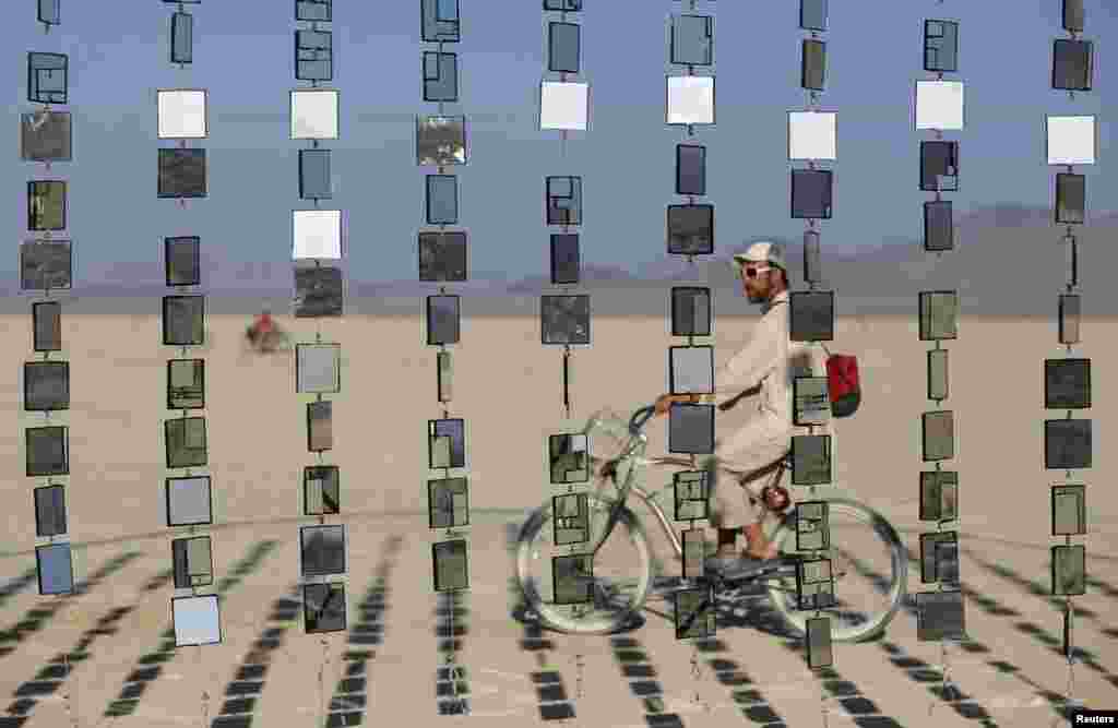 Austin Cable rides past an art installation during the Burning Man 2015 &quot;Carnival of Mirrors&quot; arts and music festival in the Black Rock Desert of Nevada, USA, Aug. 31, 2015.